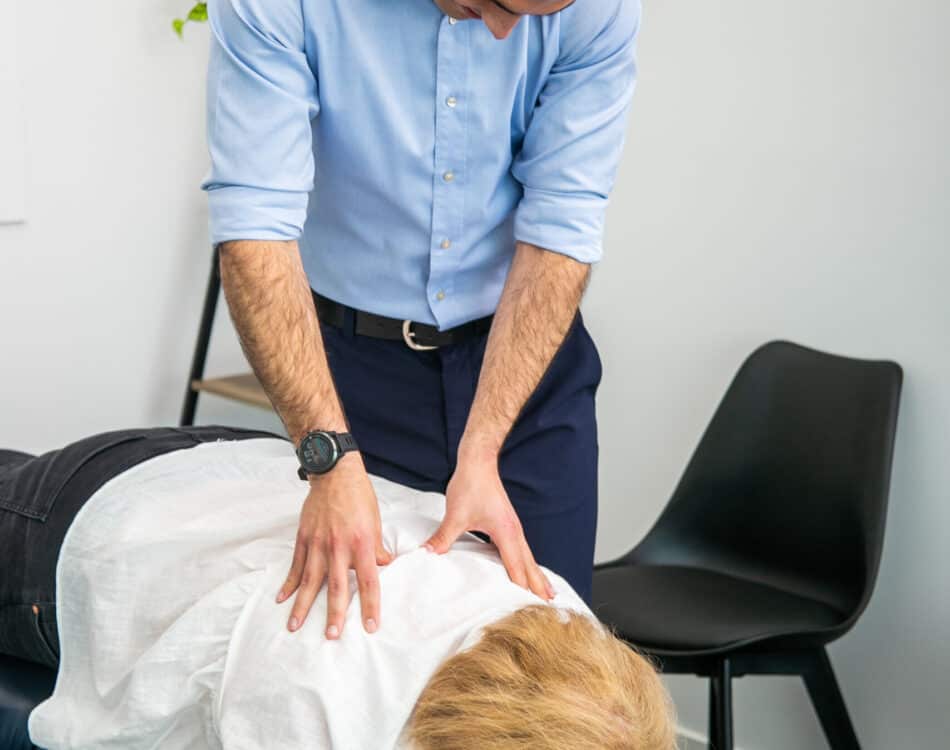 Male Geelong chiropractor performing spinal palpation examination of female client