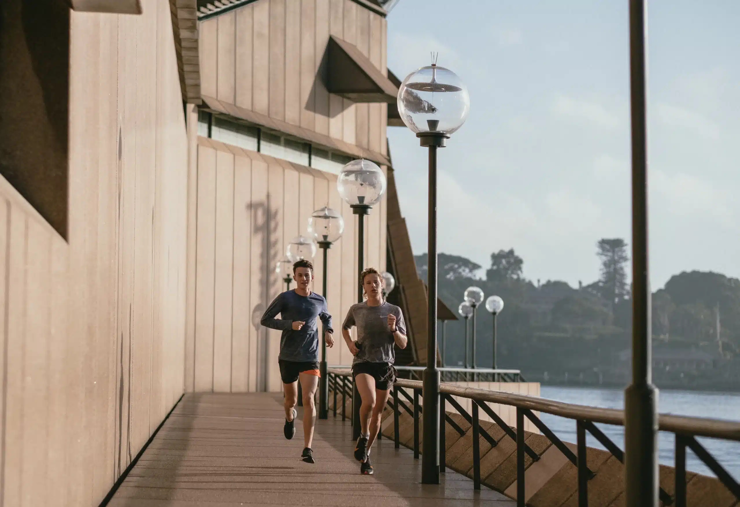 Two males running outdoors along a promenade near water