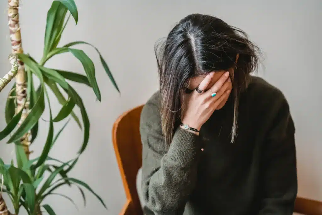dark haired woman sitting while holding her head with her hand experiencing a headache