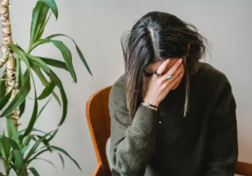 dark haired woman sitting while holding her head with her hand experiencing a headache